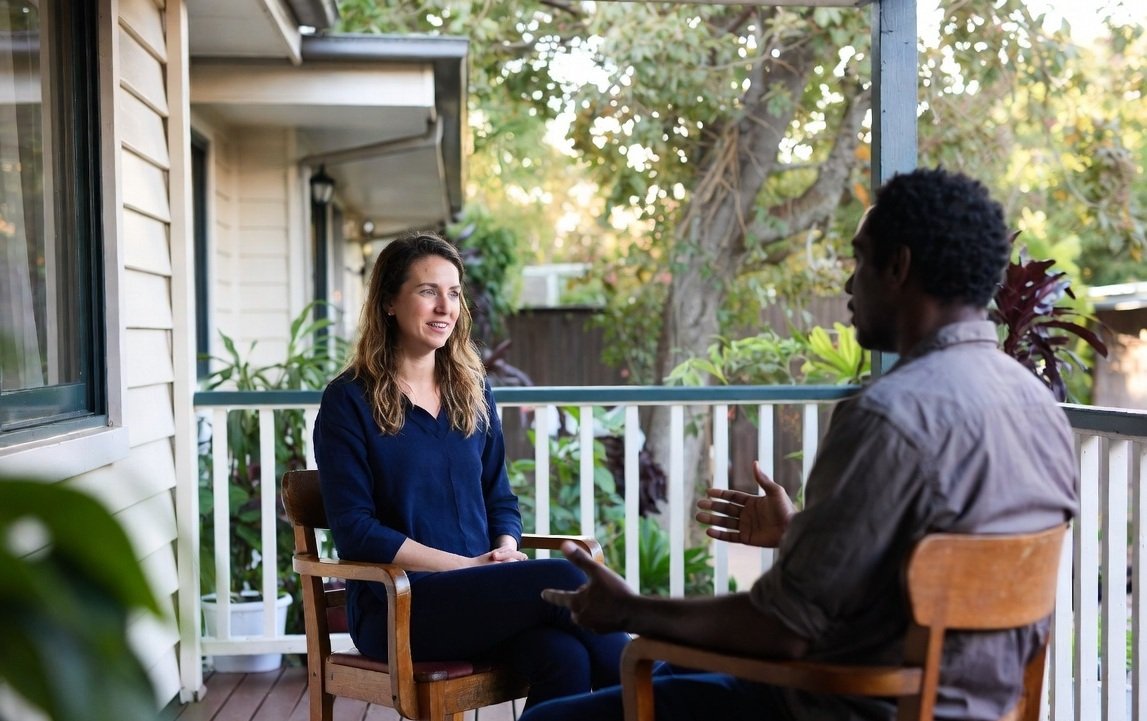 A psychosocial recovery coach and a participant talking together on a back verandah