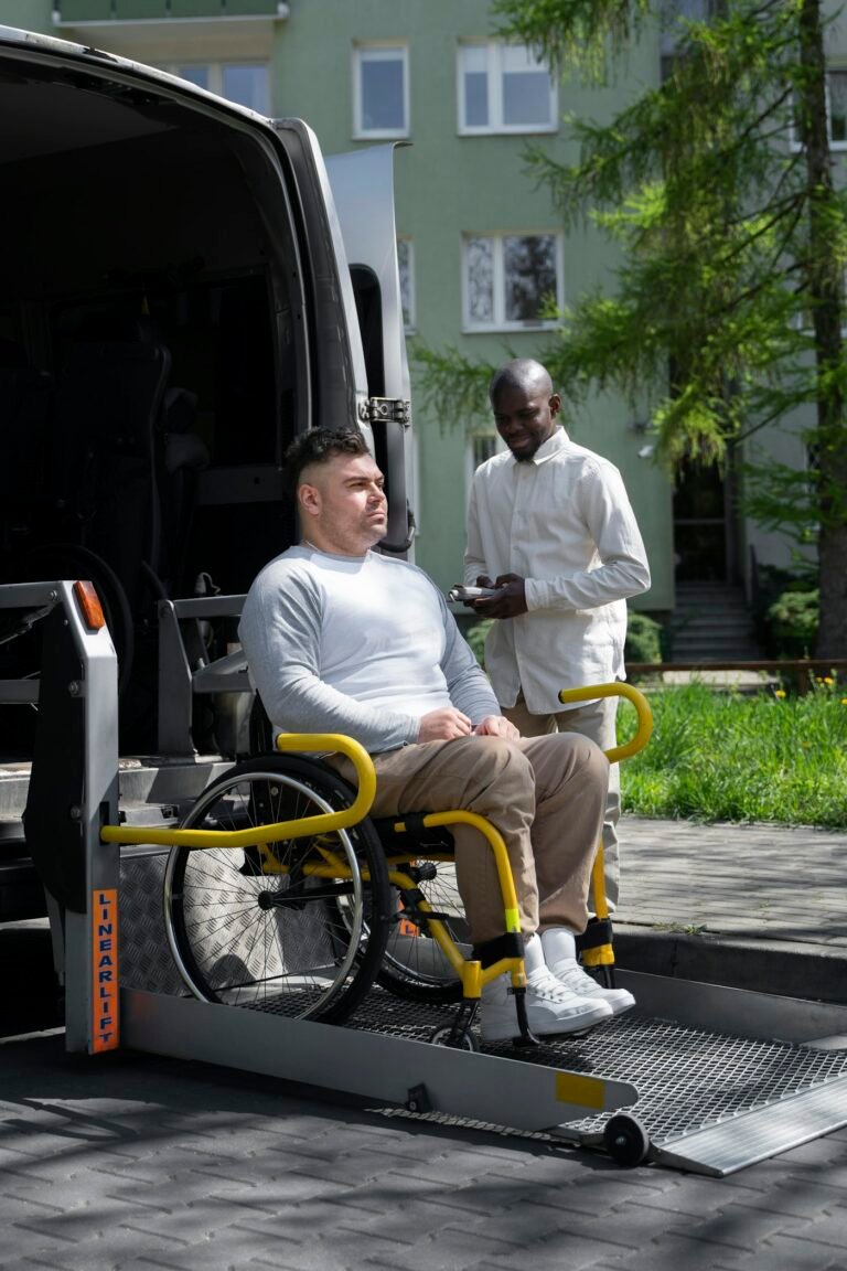 A man using a wheelchair on the lift of an accessible van, with a support worker beside him