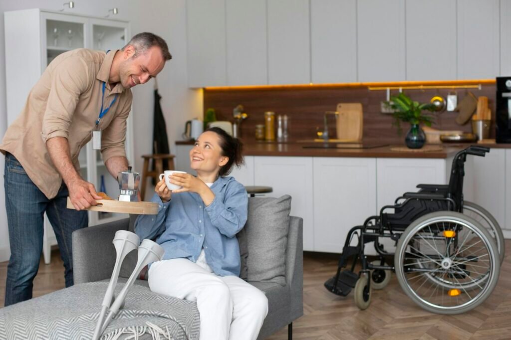 A support worker bringing a cup of tea to a woman relaxing in her living room, her wheelchair nearby